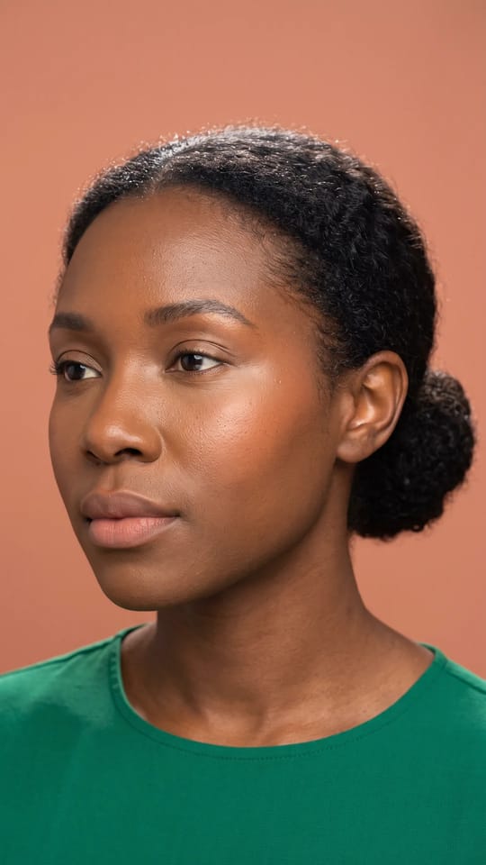 Teint cloud skin flouté : Teint cloud skin sur peau foncée : fini velours entre mat et éclat, couches fines, poudre ciblée sur la zone T, sous-ton parfaitement accordé, blush pêche et lèvres floues.