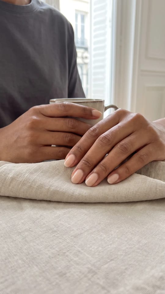 Manucure russe, cuticules nettes : Manucure russe : cuticules parfaitement dégagées et ligne de repousse nette, ongles ovales courts recouverts d'un vernis nude clair très brillant.
