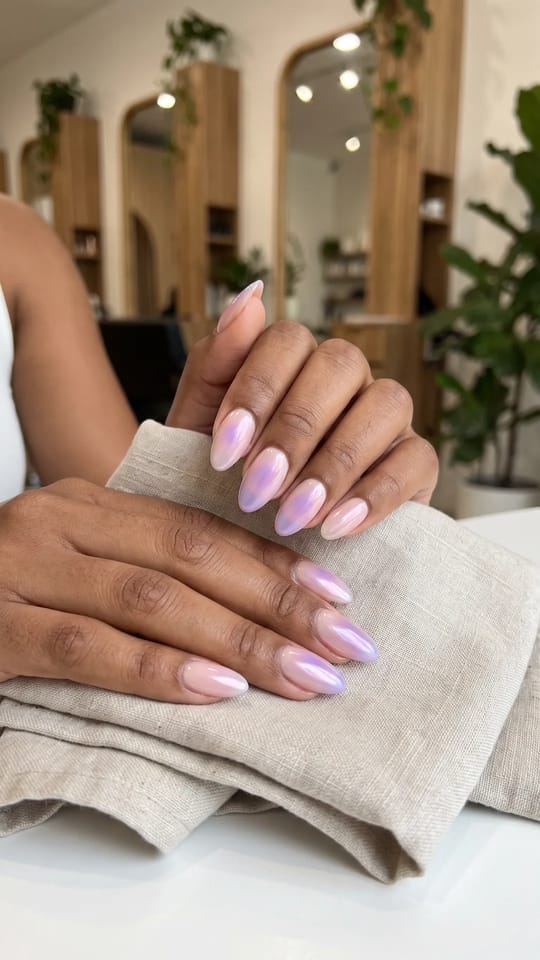 Aura nails en dégradé : Ongles mi-longs en amande avec un halo de couleur floue au centre de chaque ongle : cœur lavande qui se fond en rose pâle, puis en nude laiteux sur les bords, voile chrome nacré par-dessus.