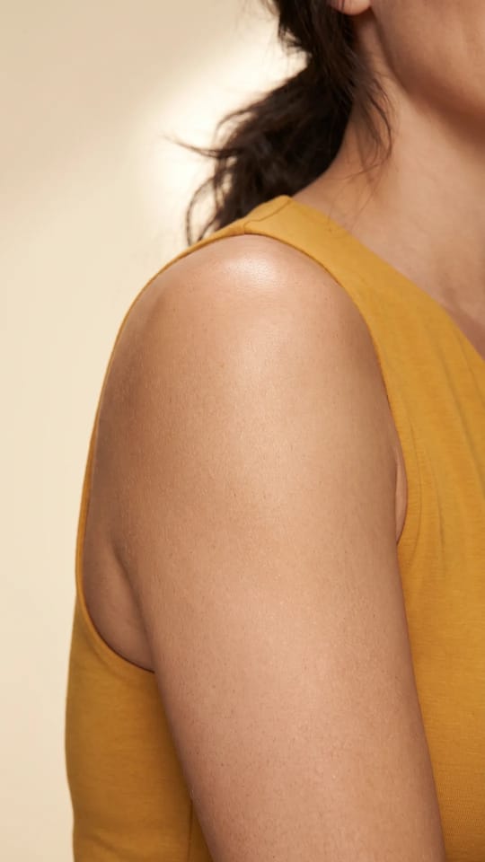 Hâle doré sur peau claire : Peau très claire teintée d'un hâle doré léger et lumineux, bras et épaules uniformes, effet vacances sans coup de soleil.